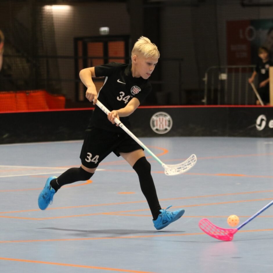 Skolēni sporta zālē spēlē florbolu